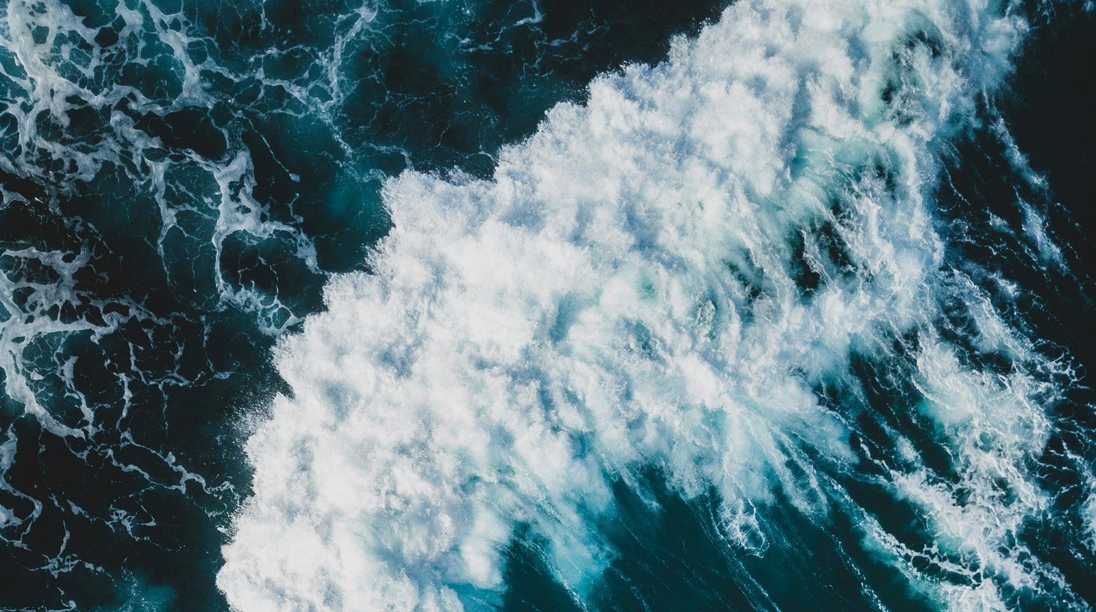 Aerial view of deep blue ocean waves creating white foam patterns along the coastline.