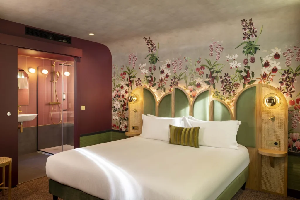 : Hôtel Jardin de Cluny guest room with a king bed, botanical wallpaper, green headboard and modern en-suite shower.