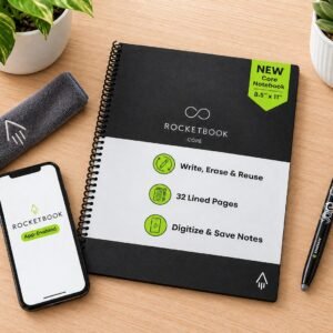 Rocketbook Core reusable notebook on a light wood desk with a smartphone, FriXion pen, cleaning cloth, and plants
