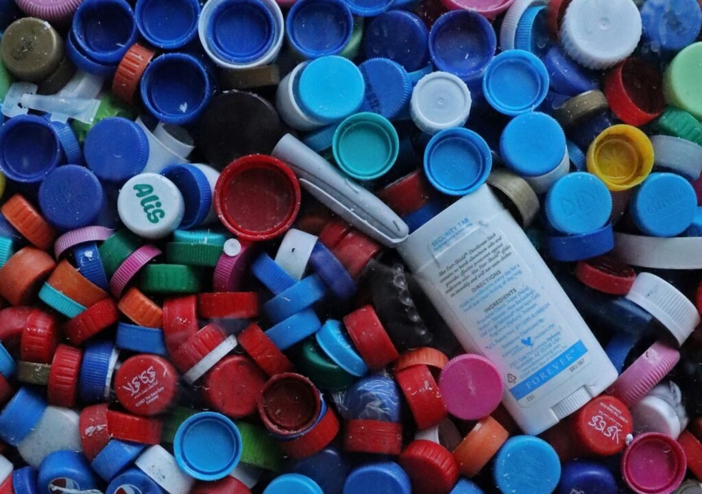 Hundreds of colorful plastic bottle caps collected in a large blue recycling bin. microplastic pollution comes from the over use of plastics