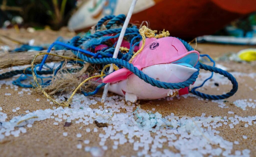 microplastic pollution and debris, tangled fishing rope, a discarded pink plastic item, and tiny plastic fragments scattered across a sandy beach