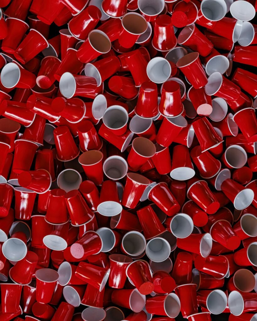 Hundreds of red disposable plastic cups piled together, illustrating the scale of single-use plastic waste.