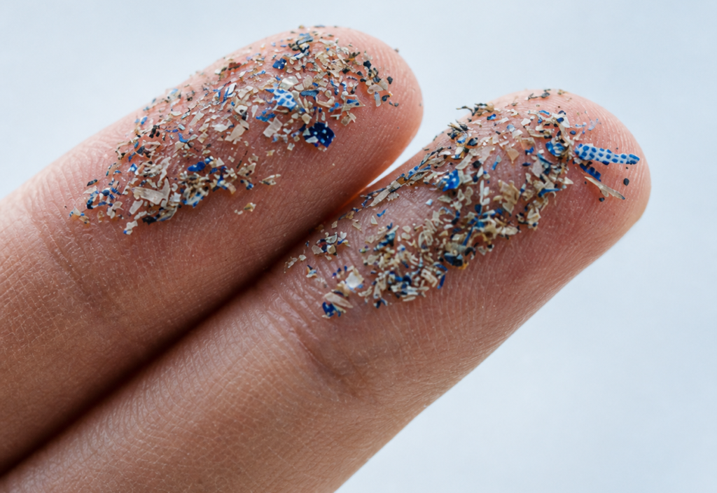 Tiny microplastic particles and pollution visible on a person's fingertips.